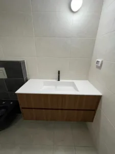 ארון אמבטיה בצבע חום מופרד לשתי חלקים עם ברז לבן ושירותים שחורים בצד