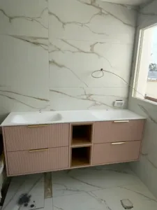 ארון אמבטיה בצבע ורוד עם ידיות זהר קיר שיש ומגירות פתוחות באמצע