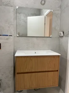 ארון אמבטיה בצבע חום עם כיור לבן על קיר בסוג שיש בצבע אפור בהיר