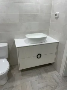 ארון אמבטיה לבן עם כיור לבן אסלה בצד שמאל שקע לצד הקיר