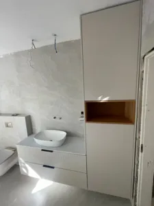 ארון אמבטיה מתחת לכיור לבן ומיצידו הימיני עם אסלה בצד שמאל