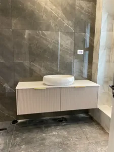 ארון אמבטיה בצבע ורוד עם ידיות זהב כיור באמצע וקיר בצבע אפור שחור צבע תואם לרצפה