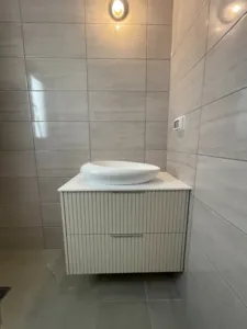 ארון אמבטיה קטן עם שתי מגירות כיור אסימטרי וקיר בצבע לבן אפור